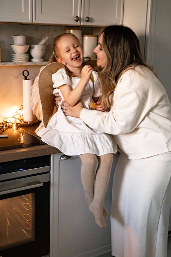 Parents kissing their little daughter in the kitchen — home Christmas session